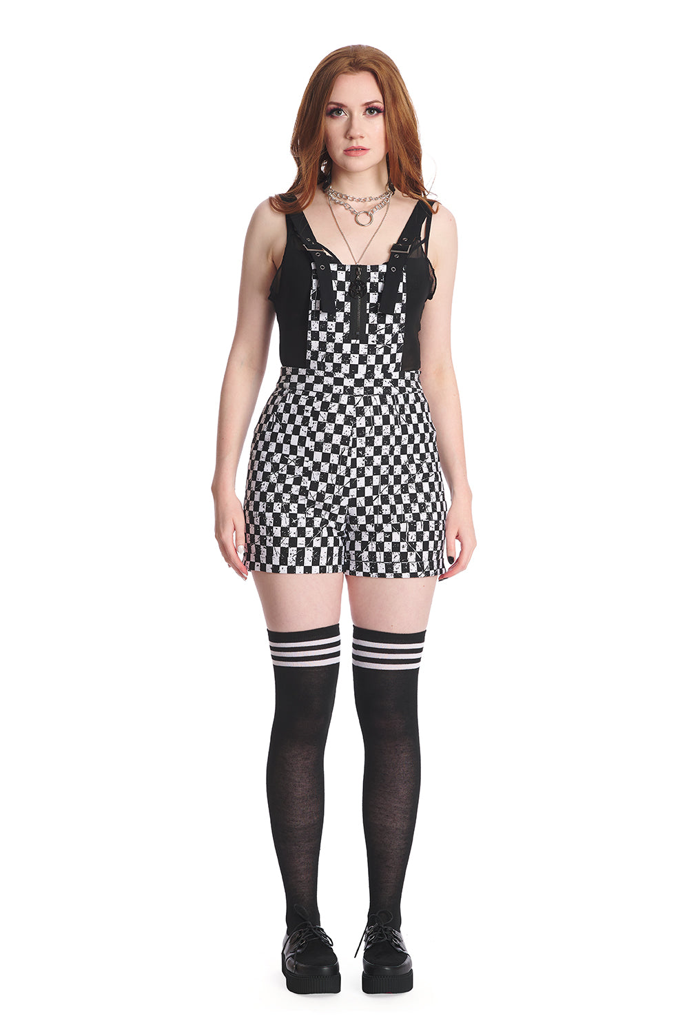 Model wears short black and white checkerboard playsuit with black vest underneath and black knee high socks.