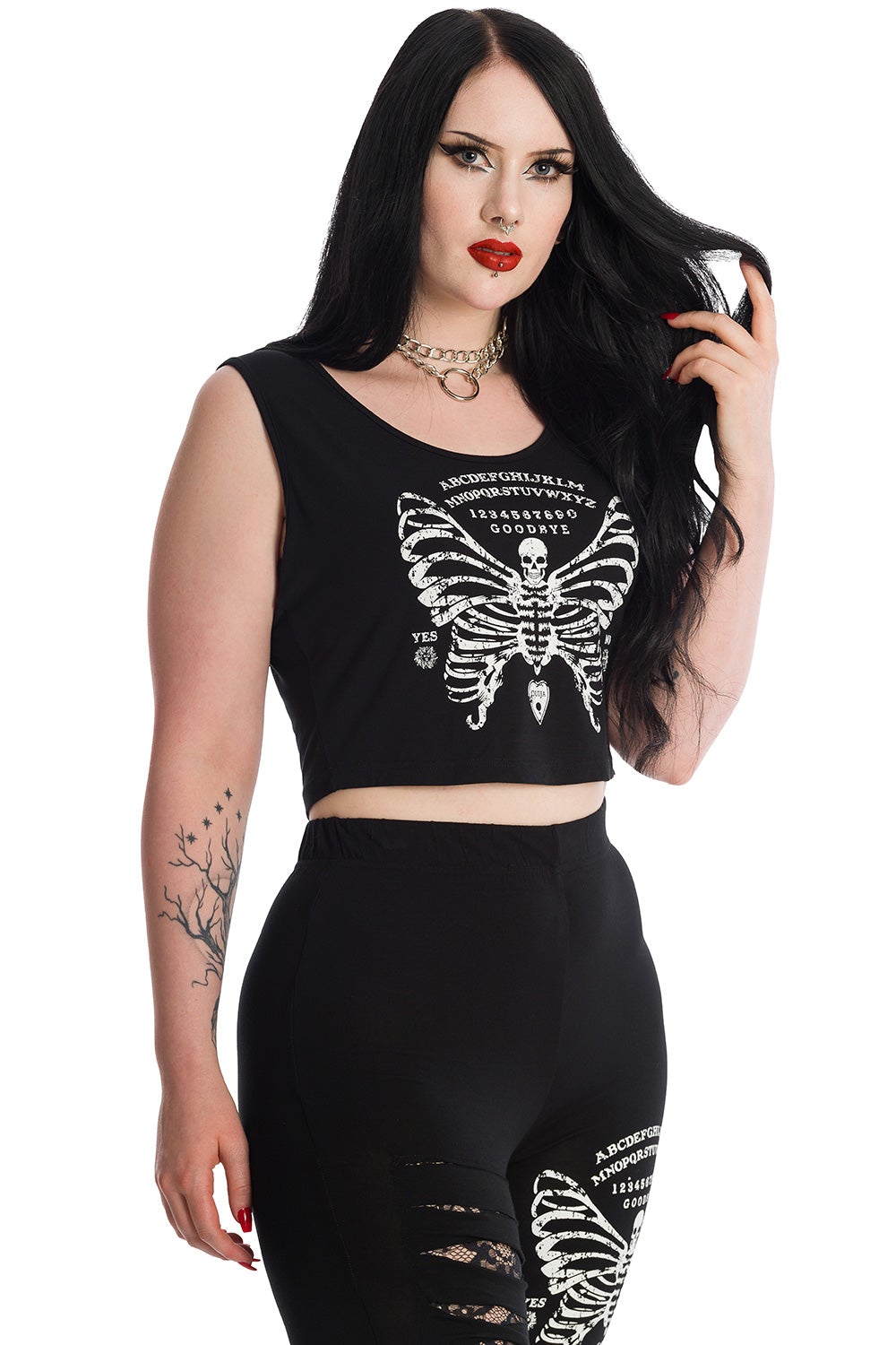 Alternative model in black sleeveless crop top with skeleton butterfly print and ouija board pattern. Model wears matching leggings.