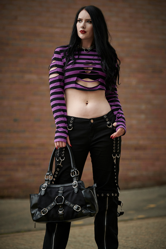 Alternative model in long sleeved crop top with ripped details in black and purple stripe and low rise grunge black trousers