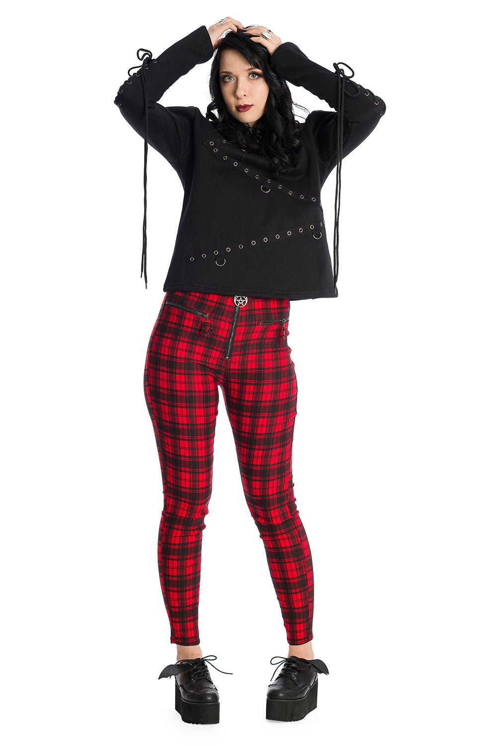 Alternative model wearing high waisted red check trousers with pentagram zip details. 