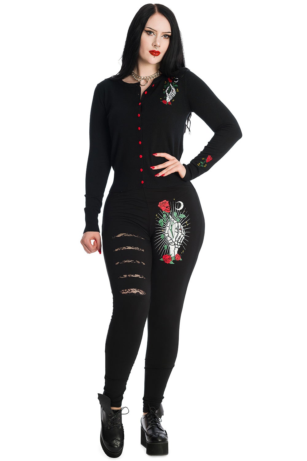 Alternative model wearing black button up cardigan with skeleton hand holding a red rose feature on left chest with matching roses on the sleeves and red buttons. Model wears matching leggings. 
