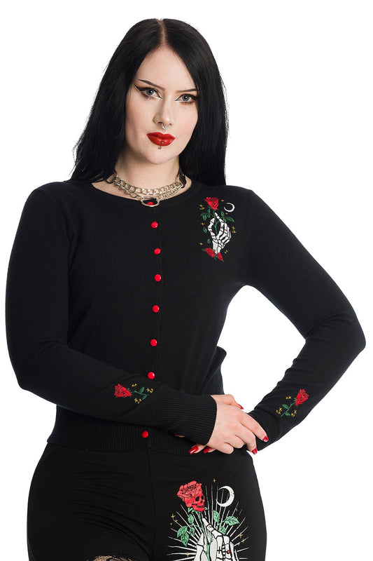 Alternative model wearing black button up cardigan with skeleton hand holding a red rose feature on left chest with matching roses on the sleeves and red buttons. 