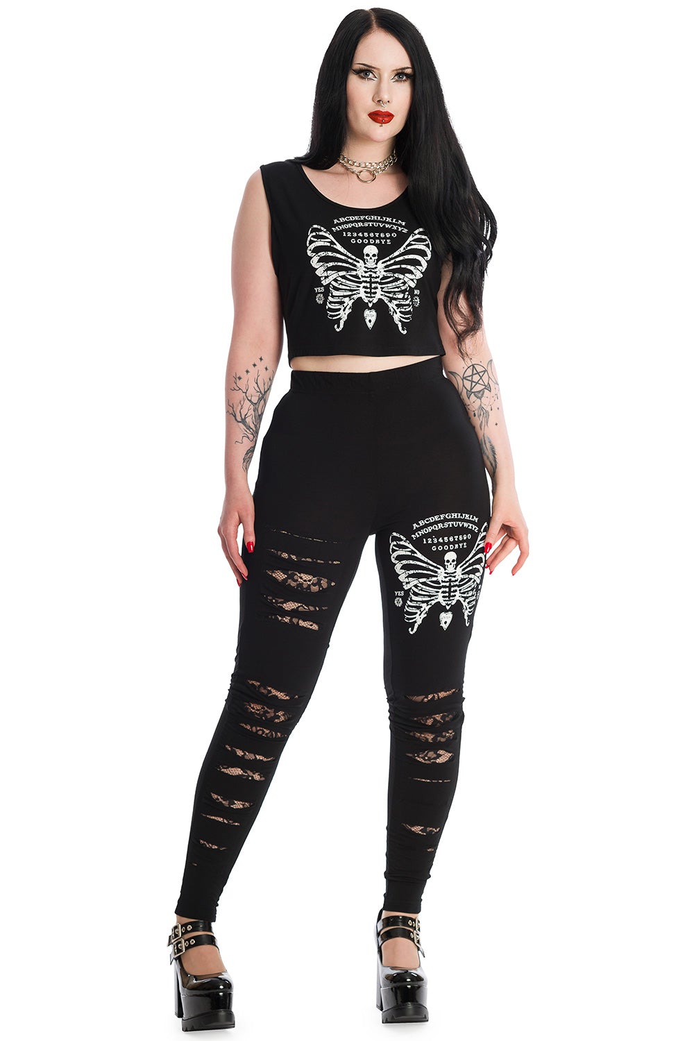Alternative model in black sleeveless crop top with skeleton butterfly print and ouija board pattern. Model wears matching leggings. 