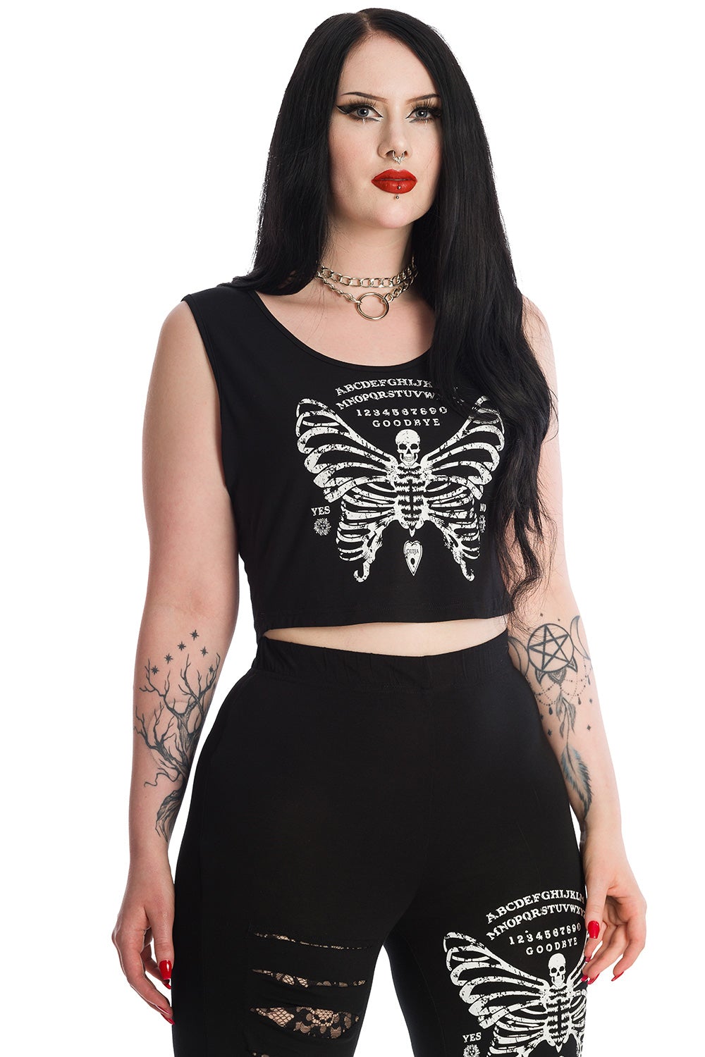 Alternative model in black sleeveless crop top with skeleton butterfly print and ouija board pattern. Model wears matching leggings. 