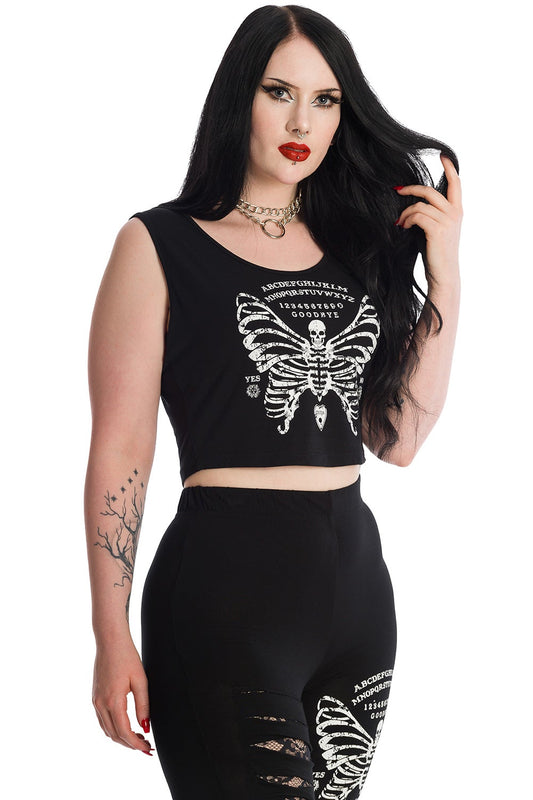Alternative model in black sleeveless crop top with skeleton butterfly print and ouija board pattern. Model wears matching leggings.
