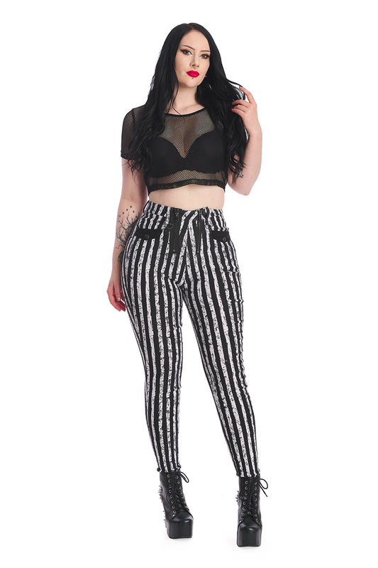 Alternative model in mesh black crop top with high waisted black and white striped skinny legged trousers with distressed colour. 